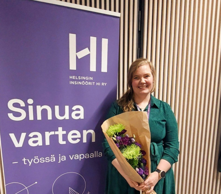 HI:n puheenjohtaja Henna Reponen yhdistyksen roll-upin edessä kukat kädessä.