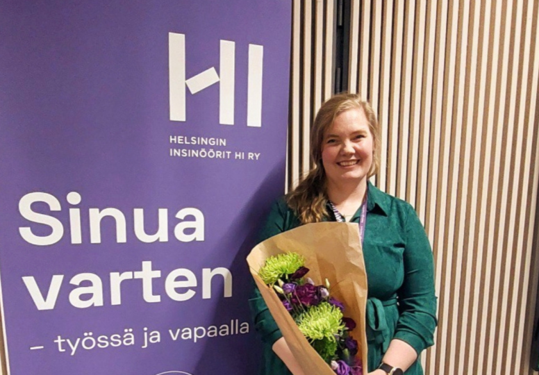 HI:n puheenjohtaja Henna Reponen yhdistyksen roll-upin edessä kukat kädessä.