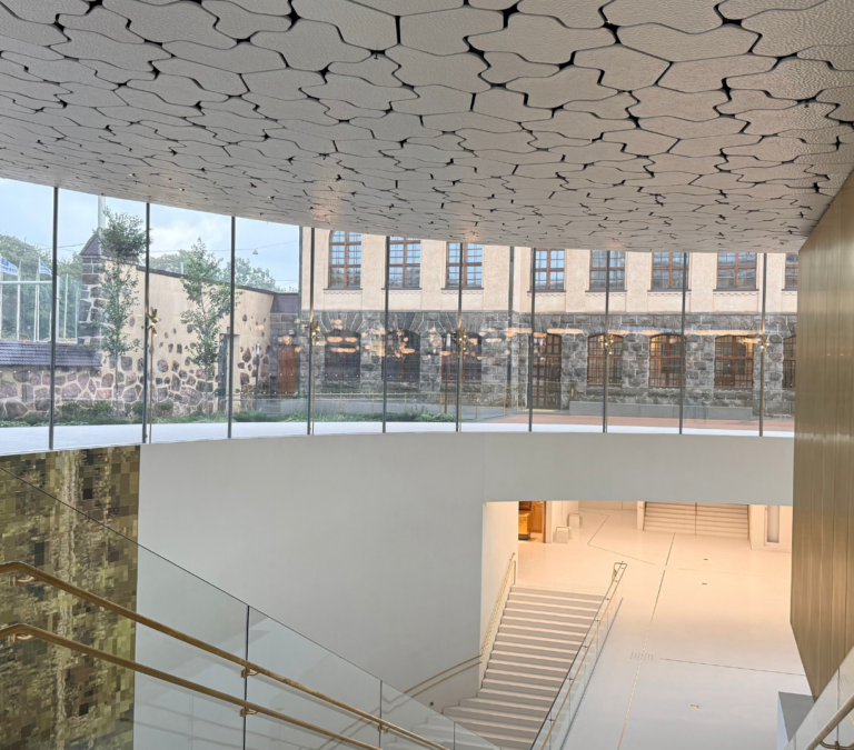 Kuva Kansallismuseon uudisrakennuksen sisältä ulos lasiseinän läpi, taustalla vanhaa päärakennusta.